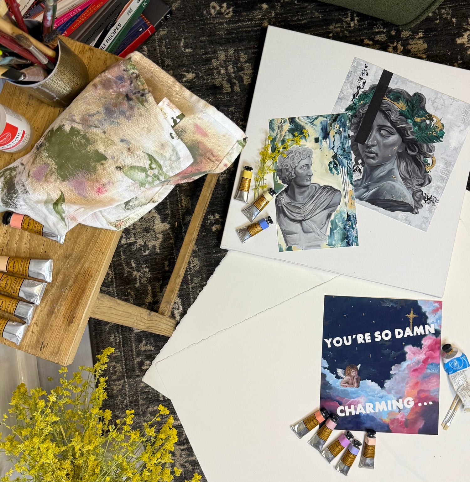 Artistic setup with paint supplies, art prints, and a motivational card on a textured surface.  By Kendelle Ashton